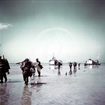 BERNIERES SUR MER(14990) 6 juin 1944 Ces soldats canadiens dbarquent sur les plages du secteur de Juno Beach, le 6 juin 1944, avec leurs quipements. En arrire-plan, deux LST dchargent leurs cargaisons d