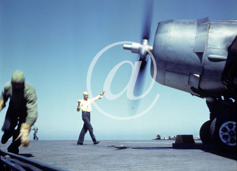 inconnu() Seconde guerre mondiale US Navy en couleurs - Srie 80-GK- : Un oprateur sur une piste de porte-avions executent ses signaux de bras devant un appareil dont le moteur tourne.
